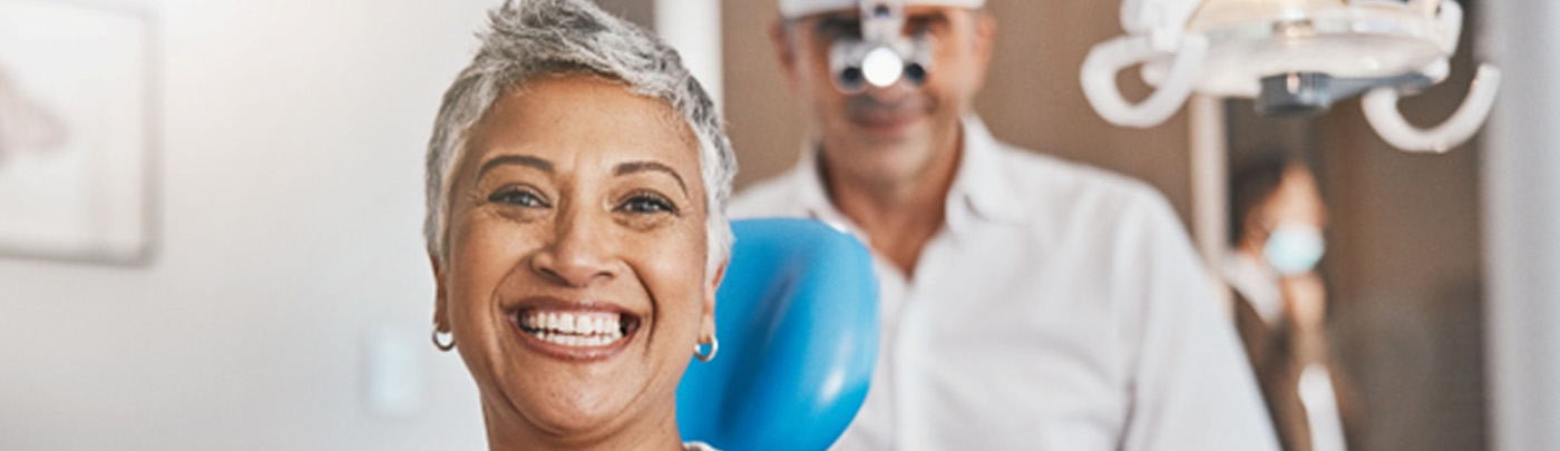 A smiling, middle-aged woman sitting in front of a dentist