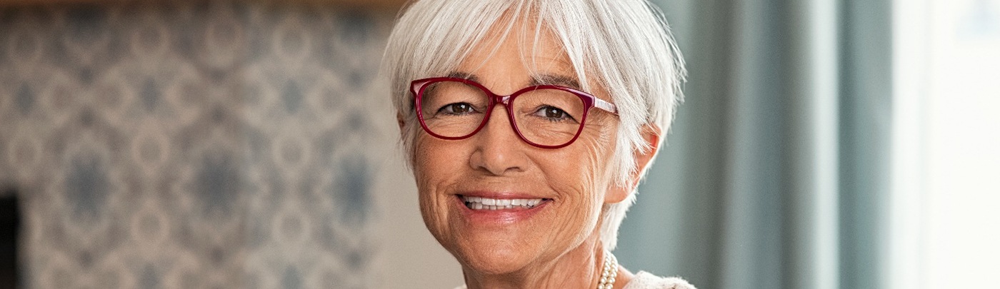 Senior woman with glasses sitting on couch and smiling with dentures in Little Elm