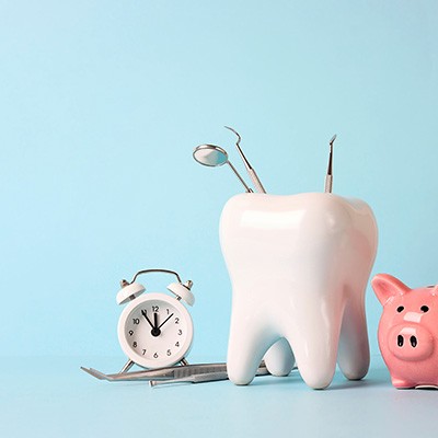 Pink piggy bank next to large model tooth containing dental instruments next to clock